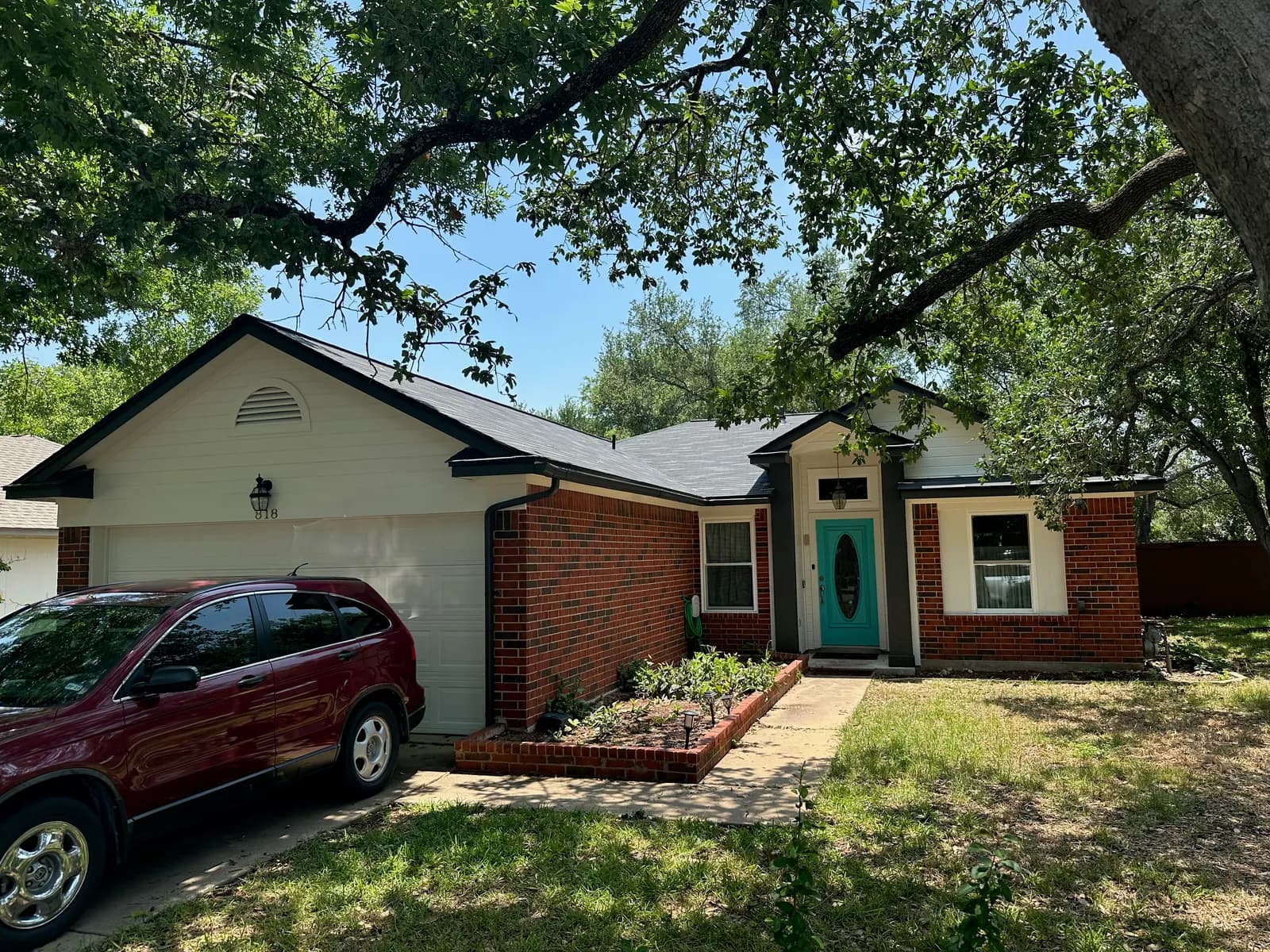 Single-story red brick ranch home with fresh black trim and a teal front door painted by Ranger Painting in Austin