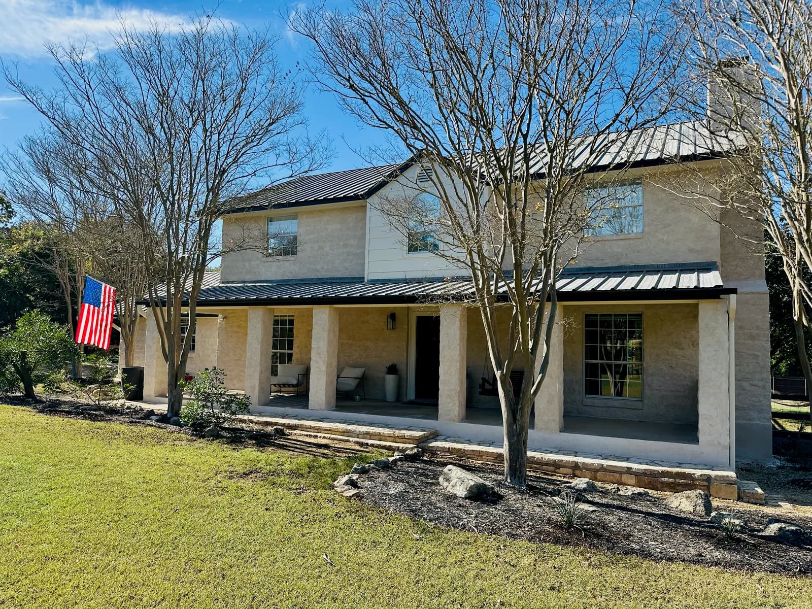 Two-story limestone Hill Country home with a metal porch roof and fresh white trim painted by Ranger Painting in Austin