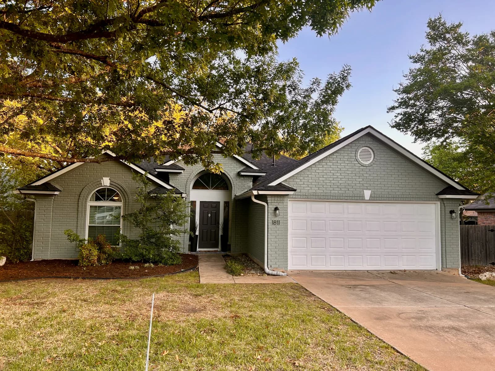 Single-story sage-green brick ranch home with a white garage door painted by Ranger Painting in Cedar Park