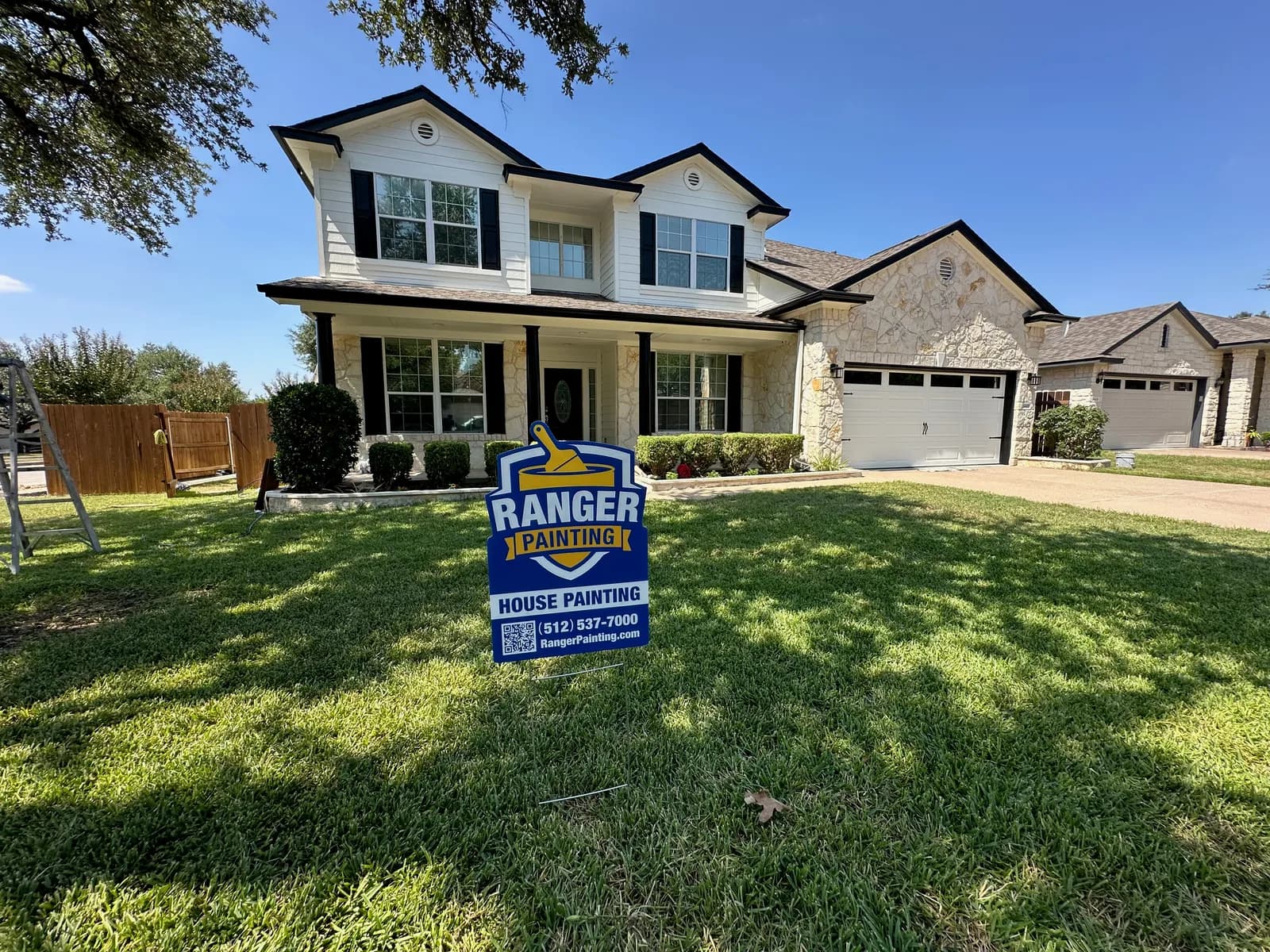 Two-story stone and stucco Austin home with crisp white trim and black shutters painted by Ranger Painting, with a yard sign in front